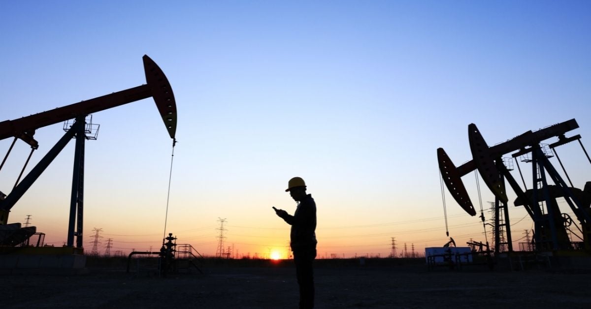 an oilfield services worker checks his phone next to an oil well pump